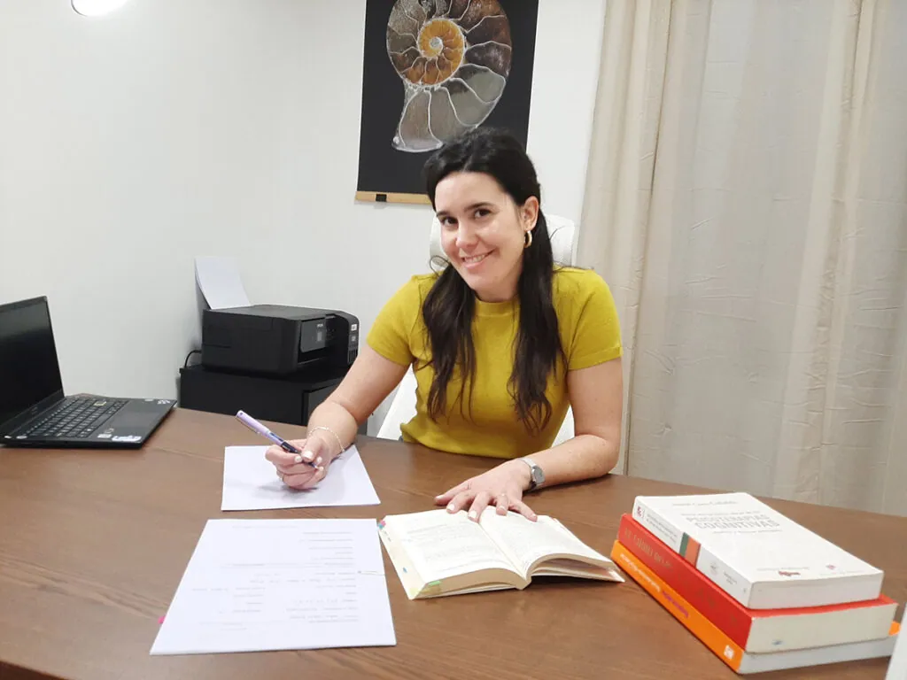 Irene Arilla en su escritorio sonriendo a cámara con varios documentos por encima de la mesa