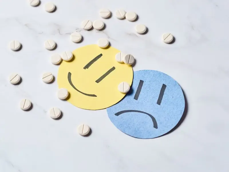 Fotomontaje con dos recortes en forma de carita sonriente y triste, con varias pastillas por encima. Ansiedad reactiva
